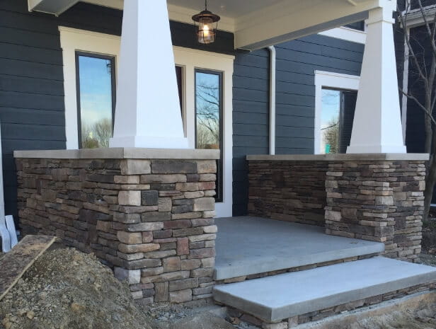Stone veneer porch with concrete steps and tapered white columns, built by Top Hat Masonry Repair